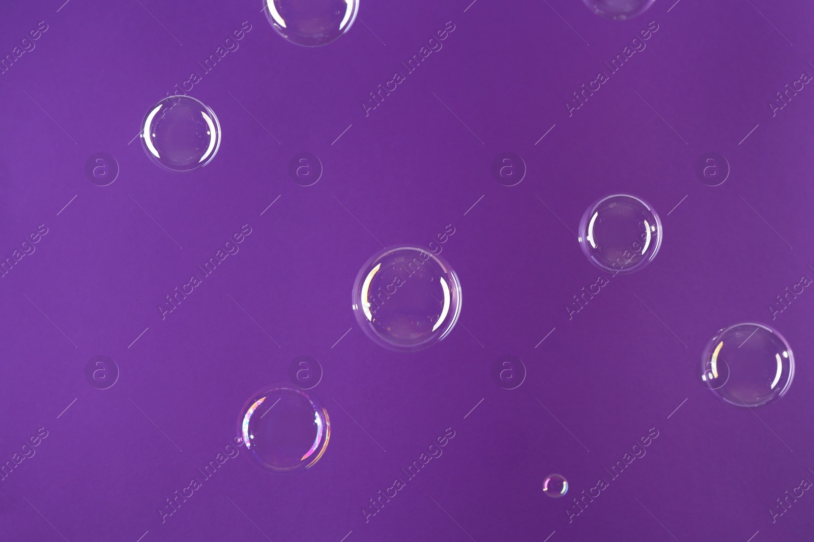 Photo of Beautiful transparent soap bubbles on violet background