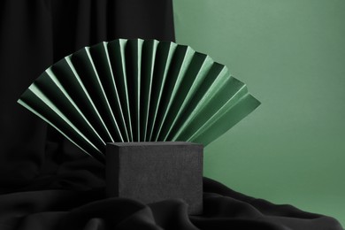 Black cube and paper fan on green background. Stylish presentation for product