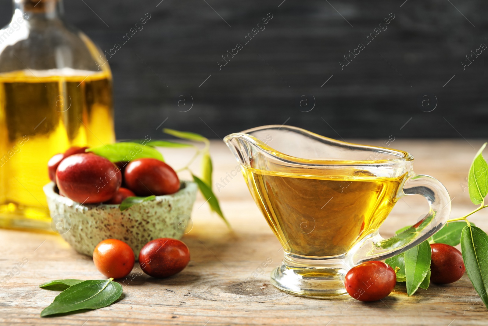 Photo of Glass sauce boat with jojoba oil and seeds on wooden table