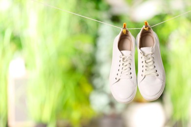 Photo of Stylish sneakers drying on washing line against blurred background, space for text