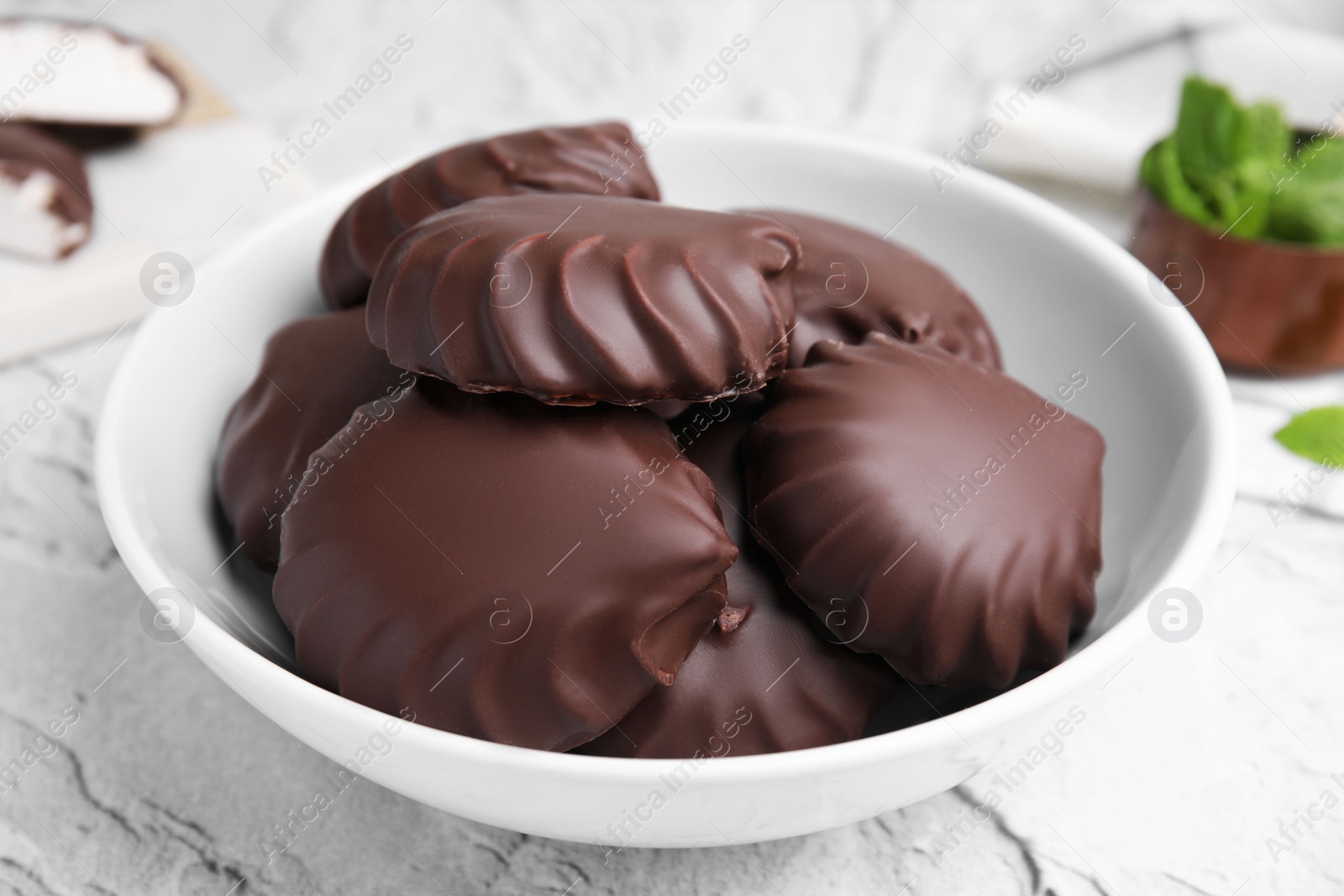 Photo of Delicious chocolate covered zephyrs in bowl on light grey table, closeup