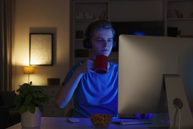 Photo of Teenage boy with cup of drink using computer in room at night. Internet addiction