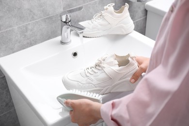 Photo of Woman washing stylish sneakers with brush in sink, closeup