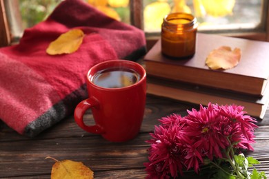 Photo of Beautiful chrysanthemum flowers, cup of tea and books on wooden table. Autumn still life