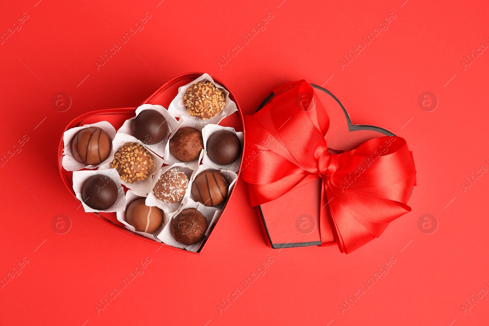 Photo of Heart shaped box with delicious chocolate candies on red table, flat lay