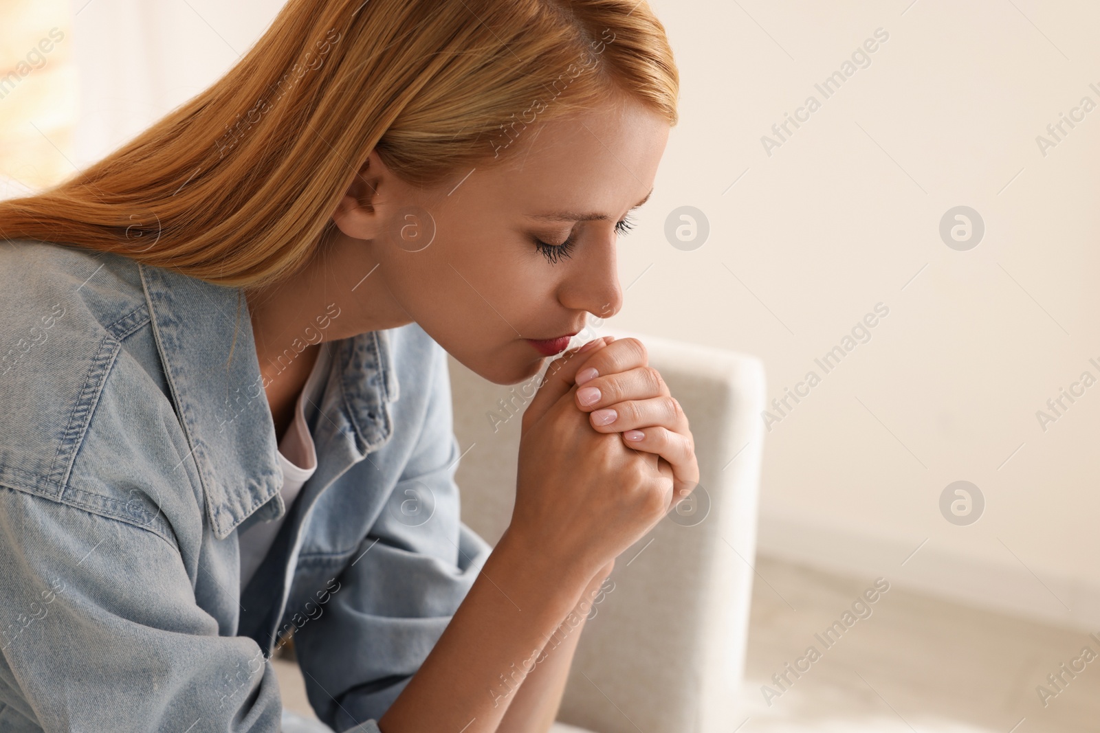 Photo of Religious young woman with clasped hands praying indoors. Space for text