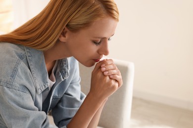 Photo of Religious young woman with clasped hands praying indoors. Space for text
