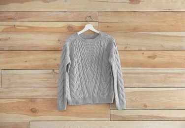 Hanger with stylish sweater on wooden wall