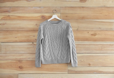 Photo of Hanger with stylish sweater on wooden wall