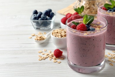 Tasty smoothie with berries, mint and oatmeal on white wooden table, space for text