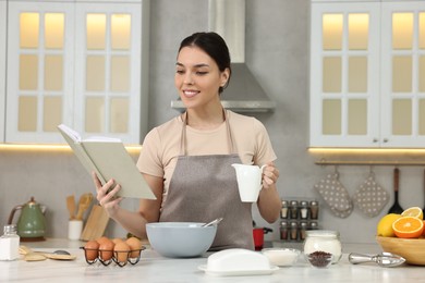 Young woman with recipe book cooking in kitchen