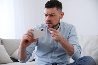 Emotional man with smartphone at home. Online hate concept