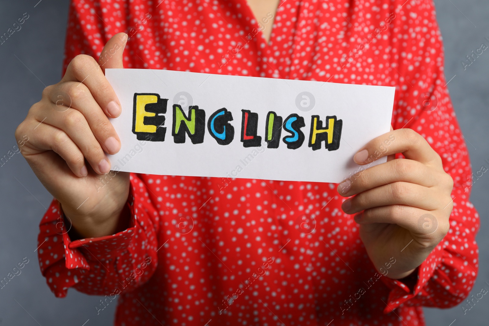 Photo of Woman holding sheet of paper with word English on grey background, closeup