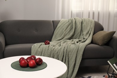 Red apples on coffee table near grey sofa with blanket indoors