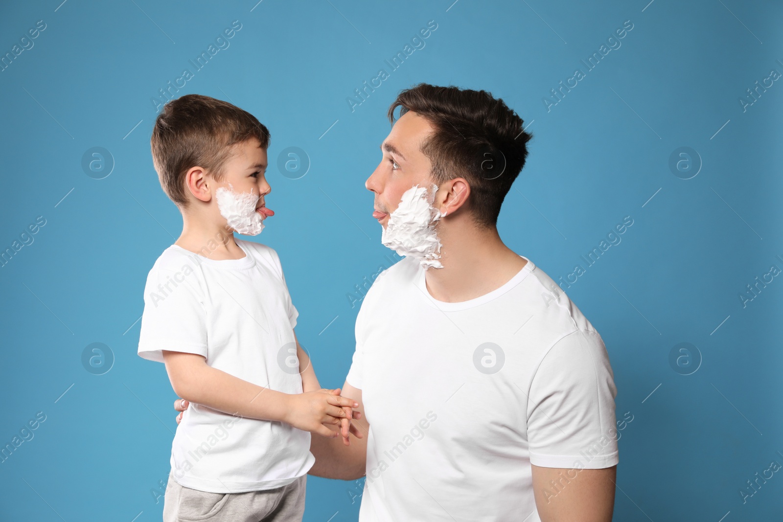 Photo of Dad and his little son with shaving foam on faces against color background