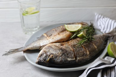 Delicious baked fish with rosemary and lime on grey table, closeup. Seafood