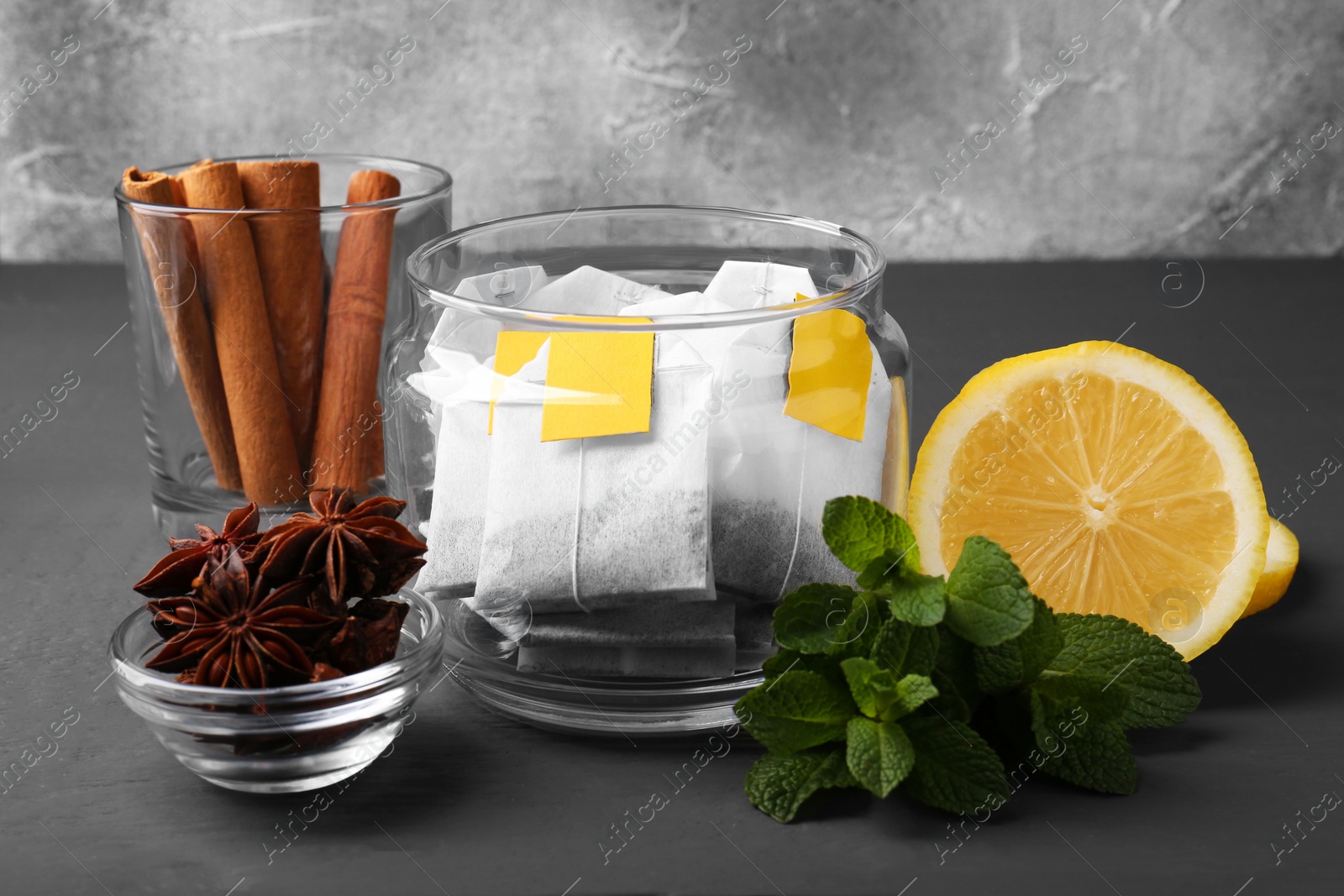 Photo of Tea bags, anise stars, cinnamon sticks, mint and lemon on grey wooden table