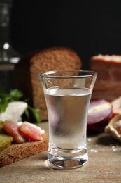 Photo of Cold Russian vodka with snacks on wooden table, closeup