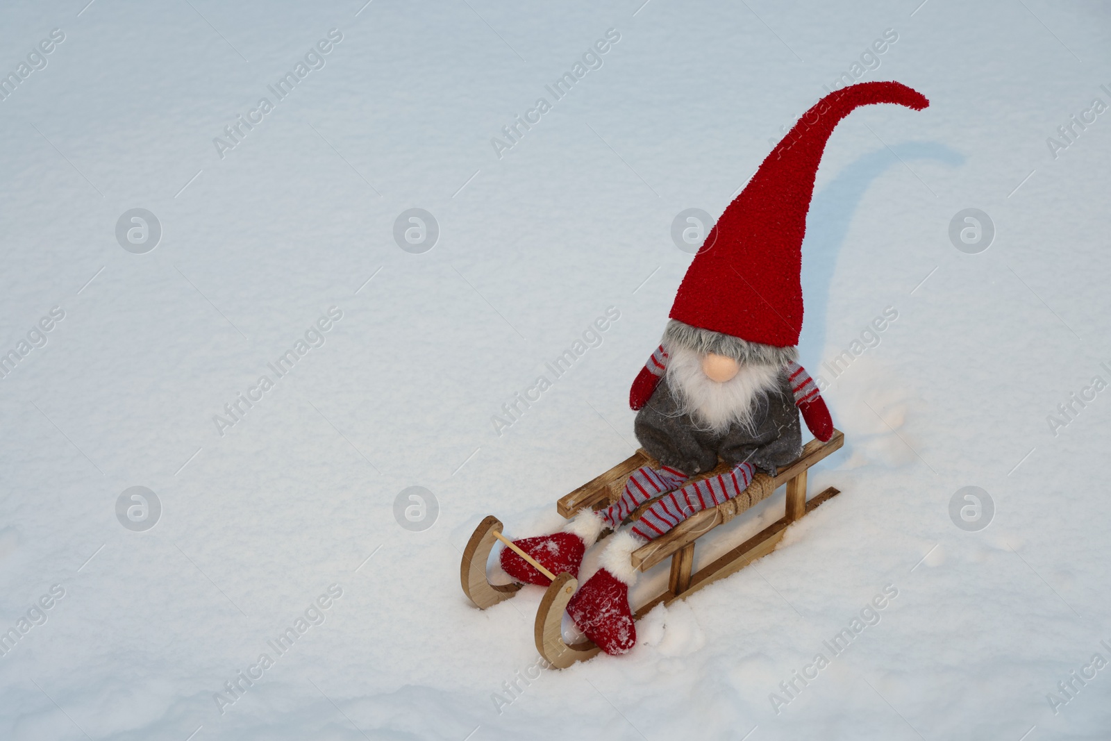 Photo of Wooden sleigh with Christmas gnome on snow outdoors. Space for text