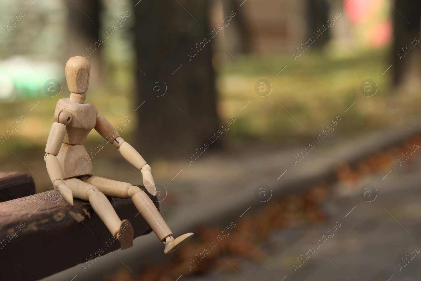 Photo of Wooden human figure sitting on bench outdoors, space for text