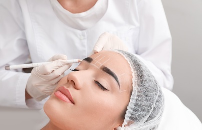 Photo of Young woman getting prepared for procedure of permanent eyebrow makeup in tattoo salon