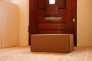 Photo of Delivery service. Cardboard on rug near wooden door indoors