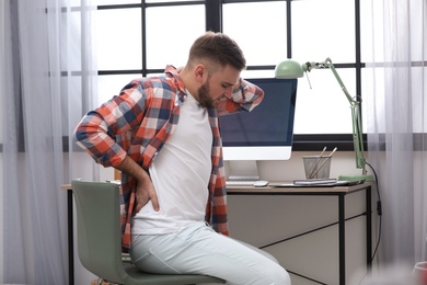 Photo of Young man suffering from back pain in office