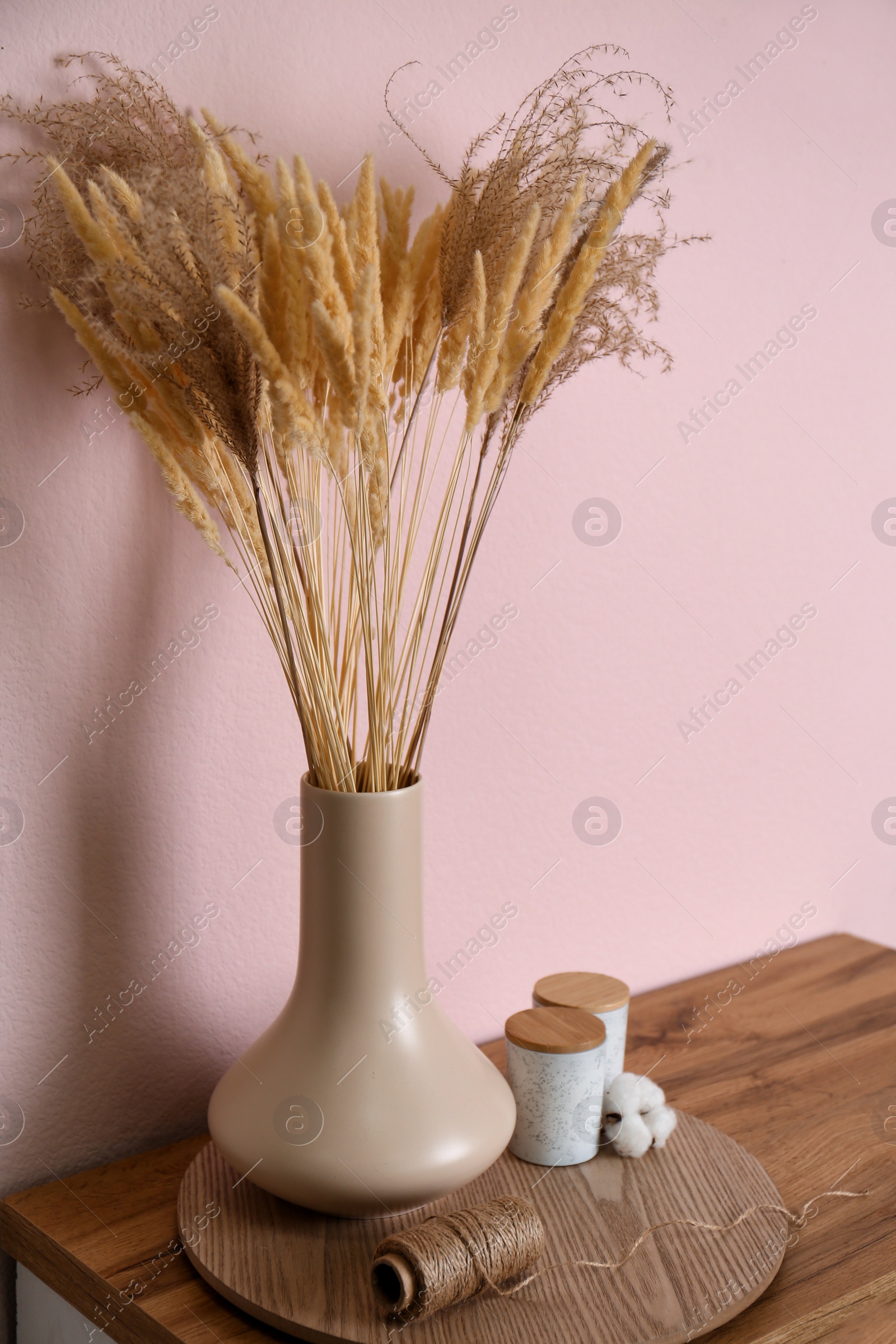 Photo of Vase with decorative dried plants on wooden table near pink wall. Interior design