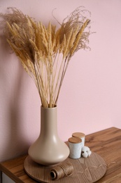 Vase with decorative dried plants on wooden table near pink wall. Interior design