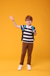 Photo of Happy schoolboy waving hello on orange background