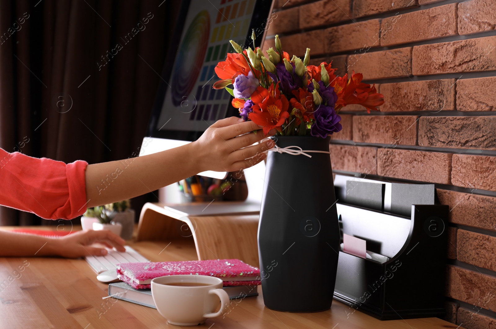 Photo of Woman with bouquet of fresh flowers in stylish vase at workplace in office, closeup