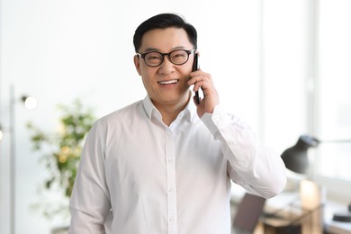 Portrait of smiling businessman talking by smartphone in office