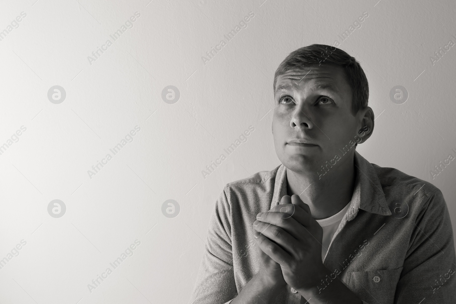 Photo of Man praying on light background with space for text. Black and white effect