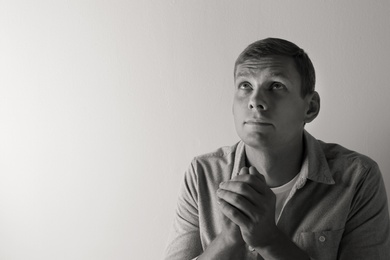 Man praying on light background with space for text. Black and white effect