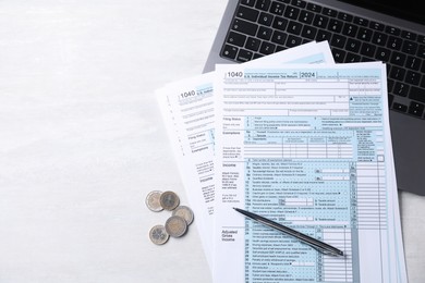 Tax forms, coins, pen and laptop on light grey table, top view. Space for text