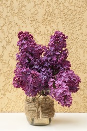 Beautiful lilac flowers in glass jar near beige wall