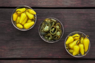 Pickled green and yellow jalapeno peppers on wooden table, flat lay