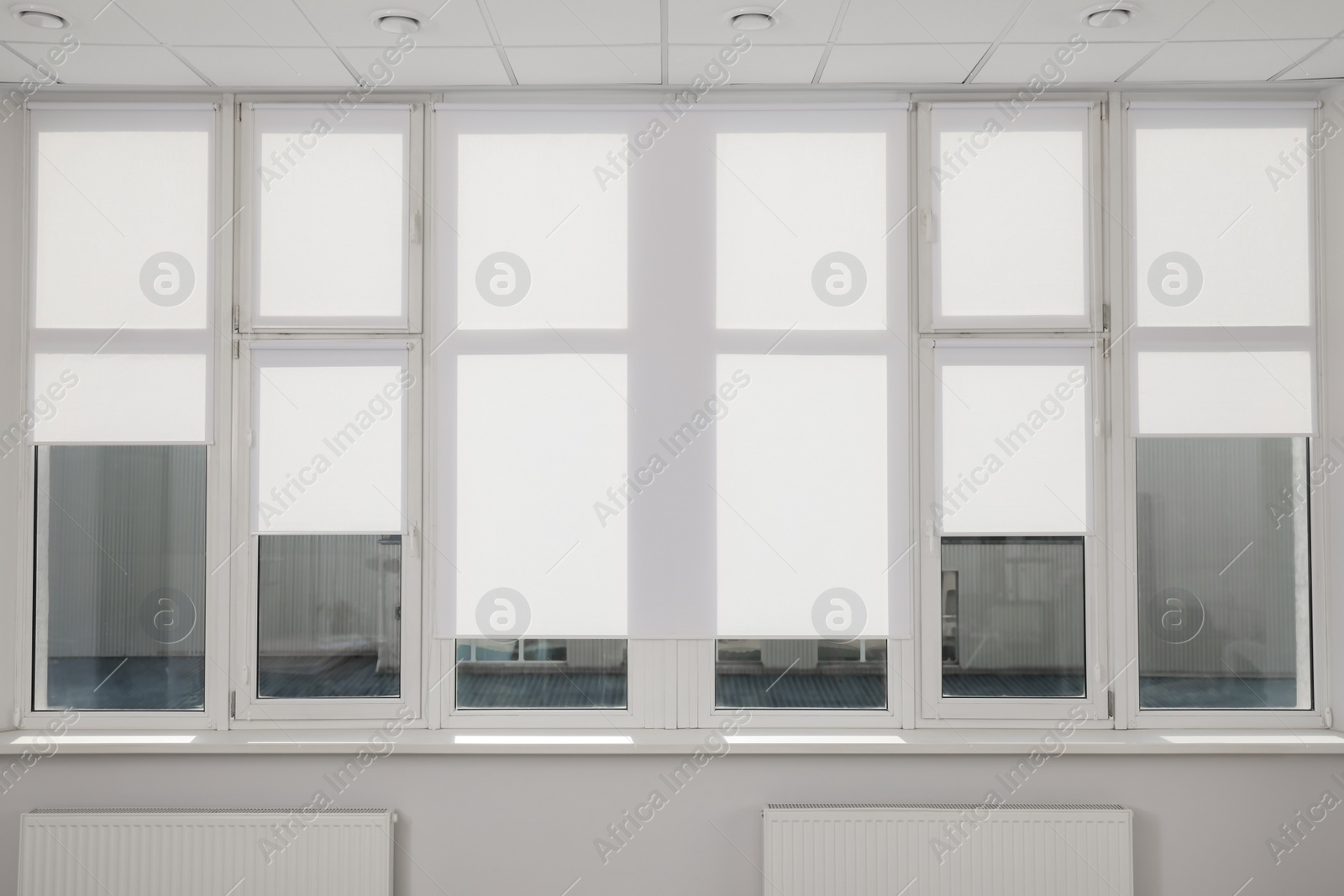 Photo of Large window with white roller blinds indoors