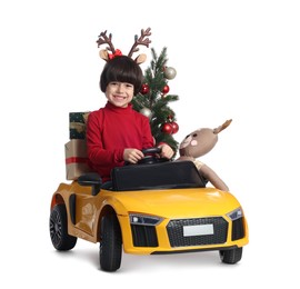 Photo of Cute little boy with Christmas tree, deer toy and gift boxes driving children's car on white background