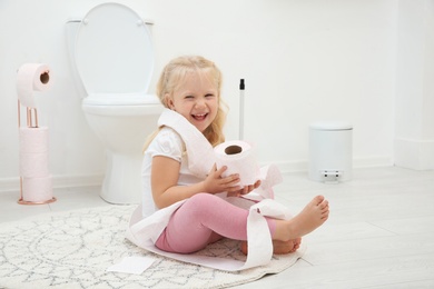 Cute little girl playing with toilet paper in bathroom