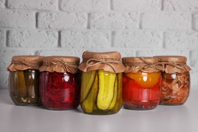 Photo of Many glass jars with different preserved vegetables on light grey table