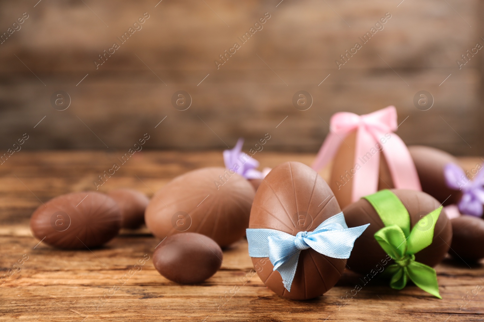 Photo of Sweet chocolate eggs with bows on wooden table. Space for text