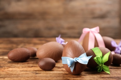 Photo of Sweet chocolate eggs with bows on wooden table. Space for text