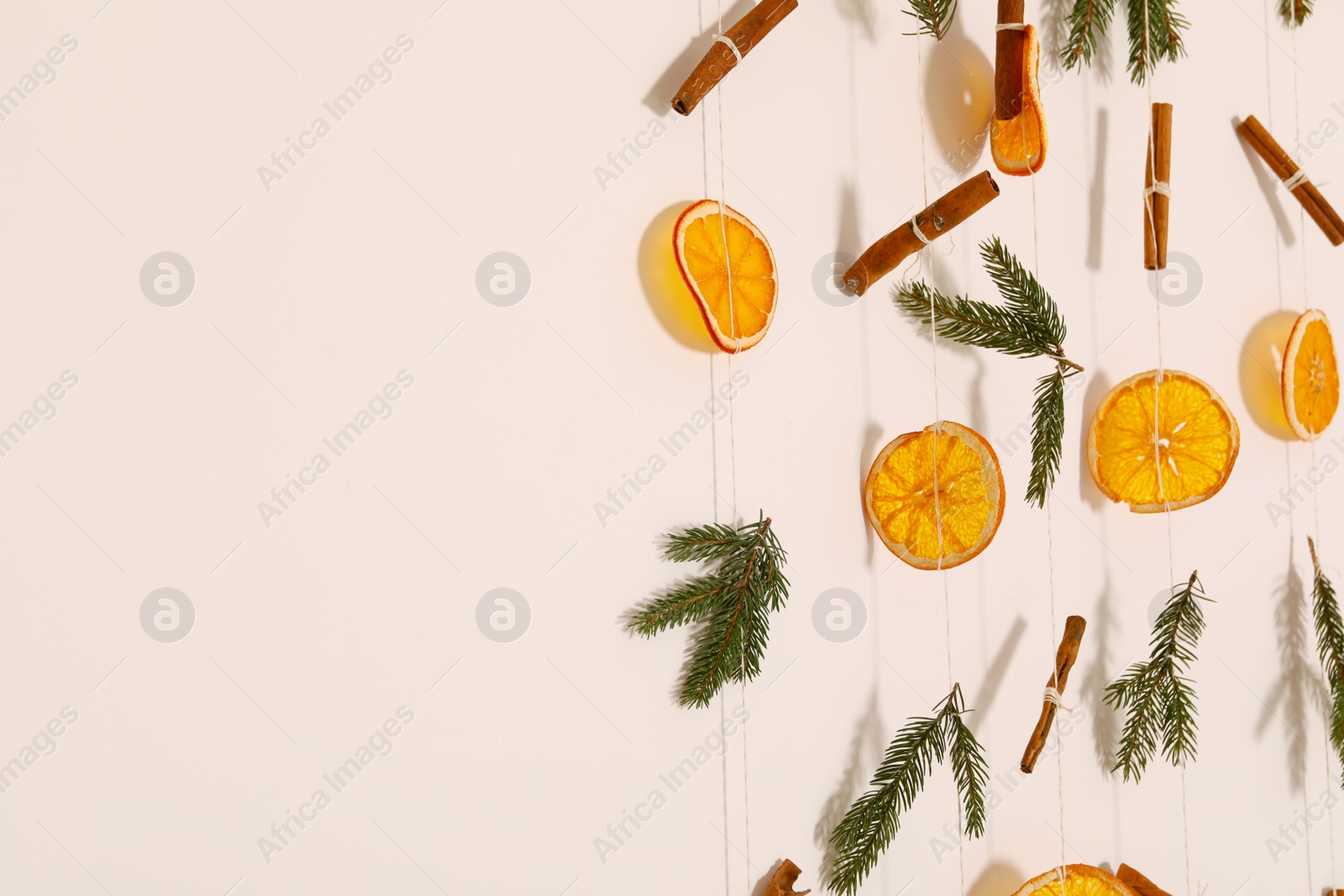 Photo of Handmade decor of dry orange slices, cinnamon sticks and fir tree branches on white wall, closeup. Space for text