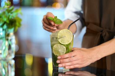 Photo of Bartender decorating glass of fresh alcoholic cocktail at bar counter