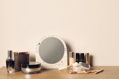 Mirror and makeup products on wooden dressing table near wall