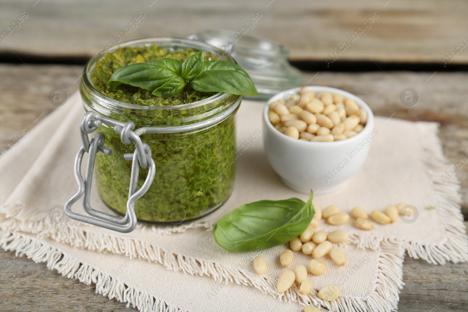 Photo of Delicious pesto sauce, pine nuts and basil leaves on wooden table, closeup