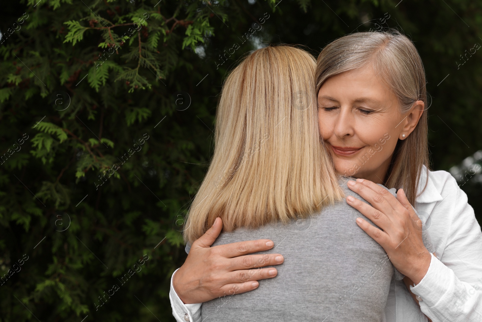 Photo of Happy mature mother hugging her daughter outdoors, space for text