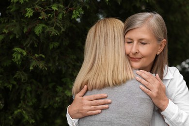 Happy mature mother hugging her daughter outdoors, space for text