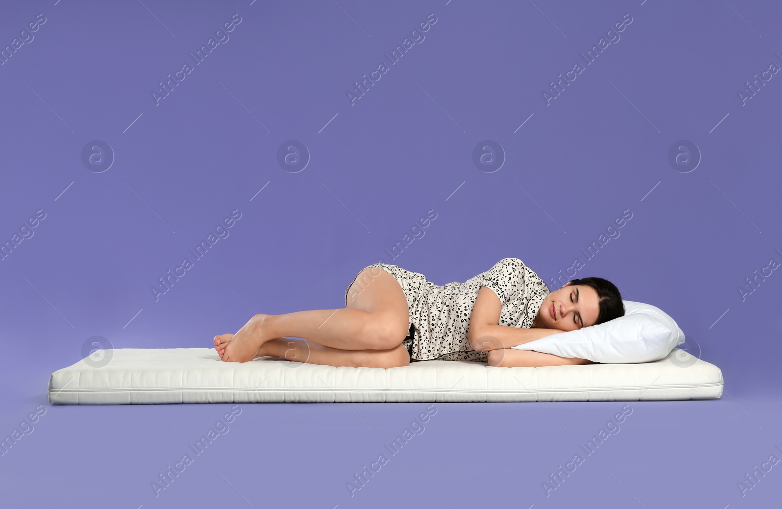 Photo of Young woman lying on soft mattress against light purple background